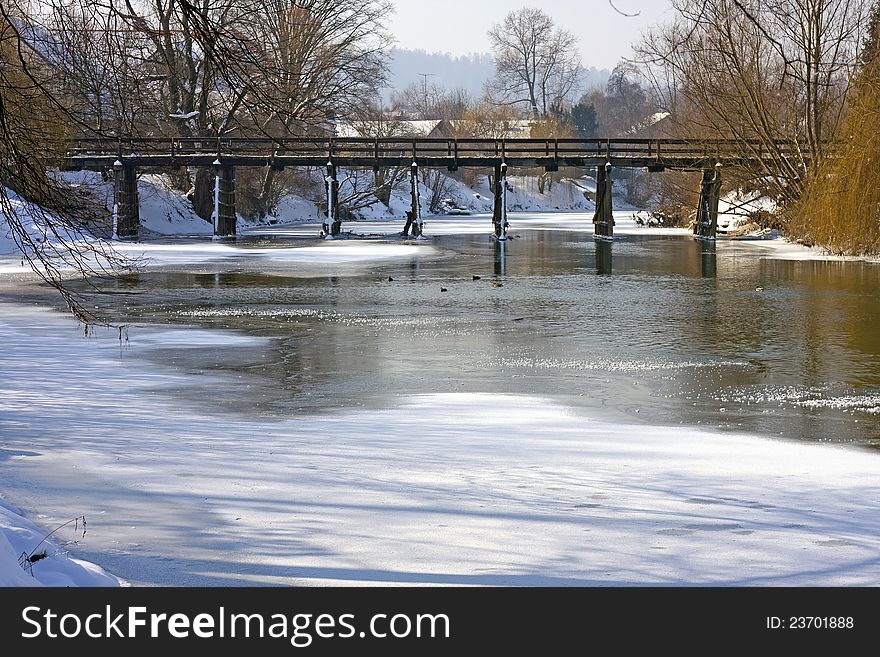 Partly frozen river with old wooden bridge in background. Partly frozen river with old wooden bridge in background.