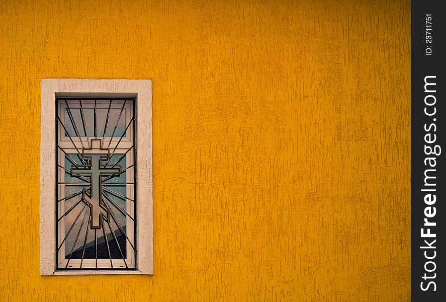 Window with grates and cross at yellow building wall