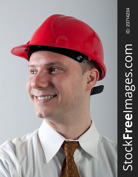 Portrait of young smiling engineer with red helmet on gray.