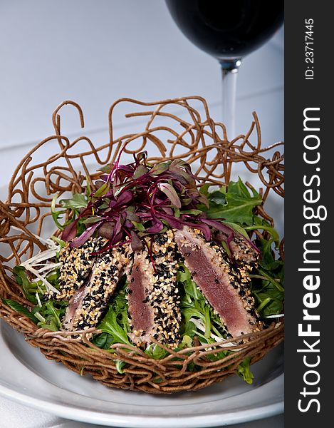 Fresh raw ahi tuna sashimi served over a green salad in an edible bowl made of noodles. All served on a white plate. Fresh raw ahi tuna sashimi served over a green salad in an edible bowl made of noodles. All served on a white plate.