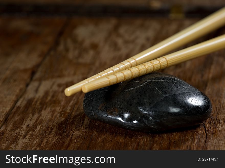 Close up of a pair of light chopsticks resting on a black stone on a rustic wood table. Close up of a pair of light chopsticks resting on a black stone on a rustic wood table.