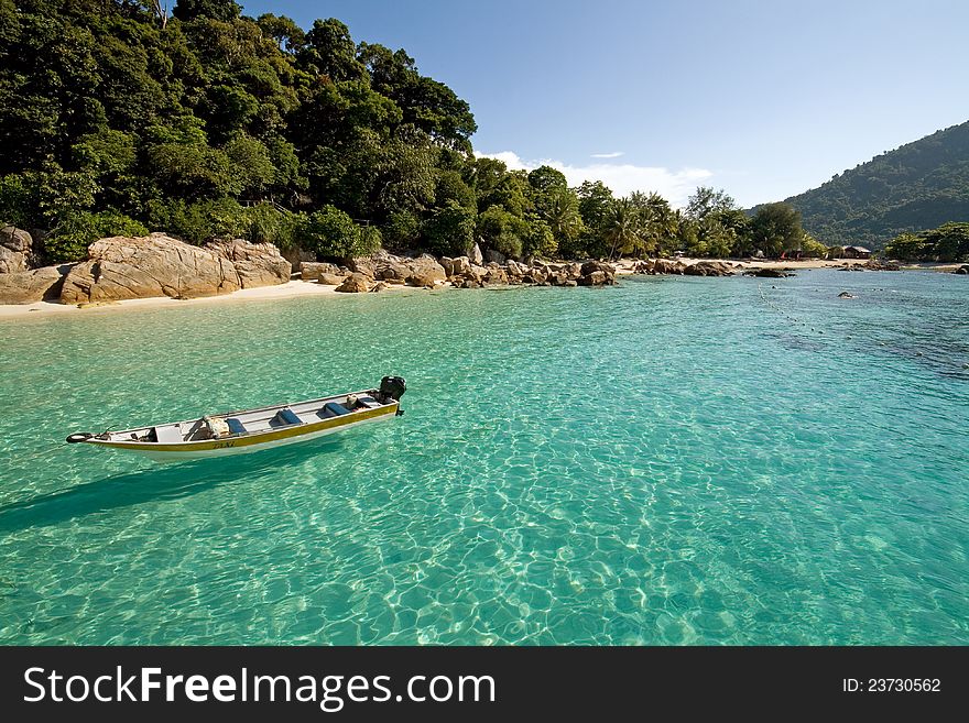 Boat floating at crystal clear waters next to a paradise island in Malaysia.