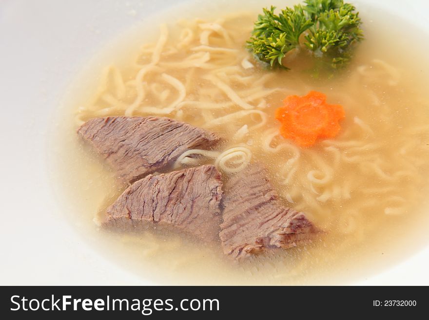 Beef broth with noodle soup in a white dish over the frame