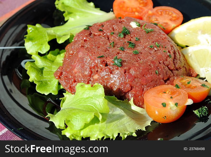 Raw ground beef with vegetables on a black dish