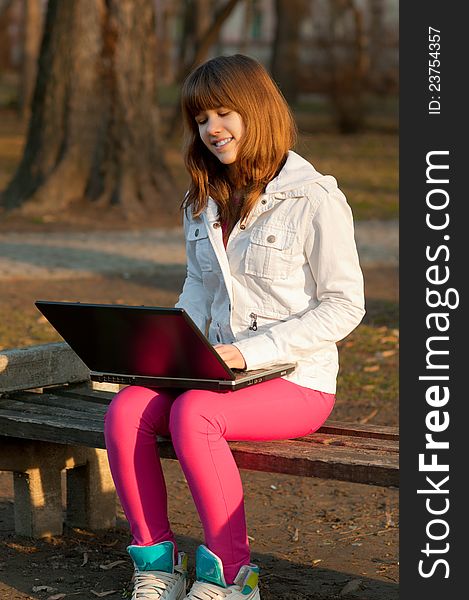 Pretty smiling teenage girl typing on notebook in the park on sunny spring day. Pretty smiling teenage girl typing on notebook in the park on sunny spring day.