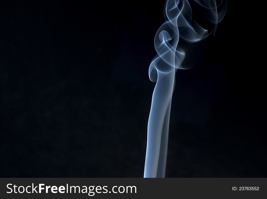 Burning incense smoke spirals on black background