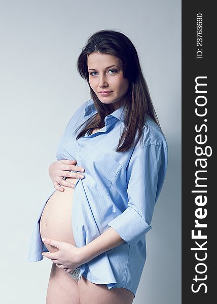 Beautiful pregnant white woman wearing blue shirt. Long dark hair. Hands on belly. Pregnancy collection.