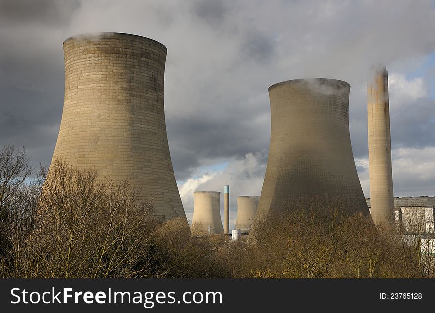 Giant cooling towers at an electricity generating station. White steam against a moody sky with winter sun. Giant cooling towers at an electricity generating station. White steam against a moody sky with winter sun.