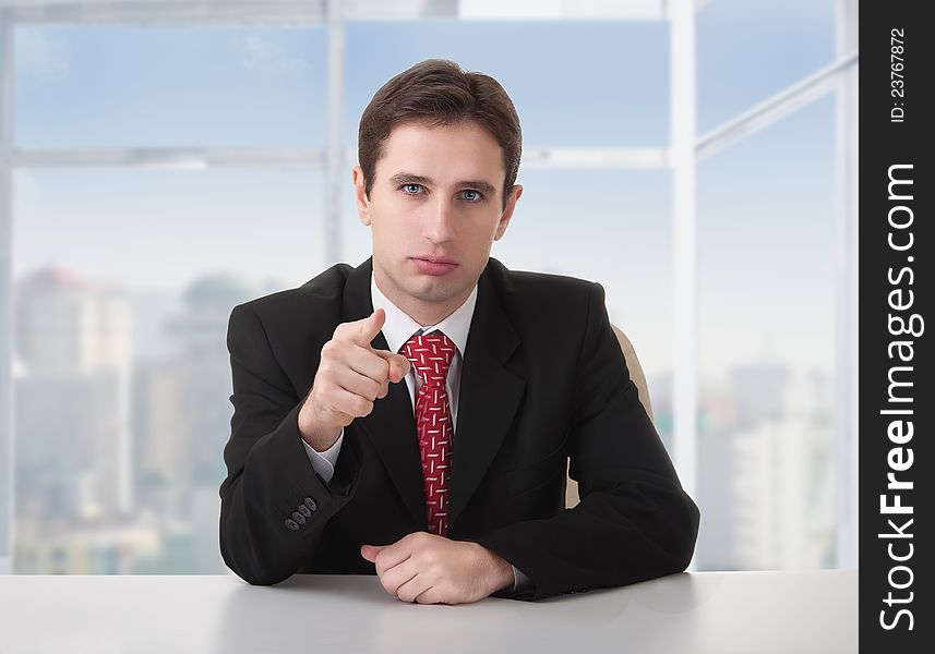 Successful businessman seriously sitting at a desk in his office and shows the index finger of the hand. Successful businessman seriously sitting at a desk in his office and shows the index finger of the hand