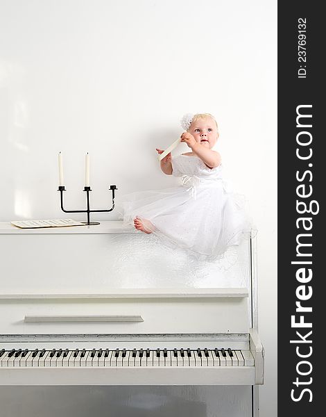 A girl in white dress sitting on a piano in the room. A girl in white dress sitting on a piano in the room