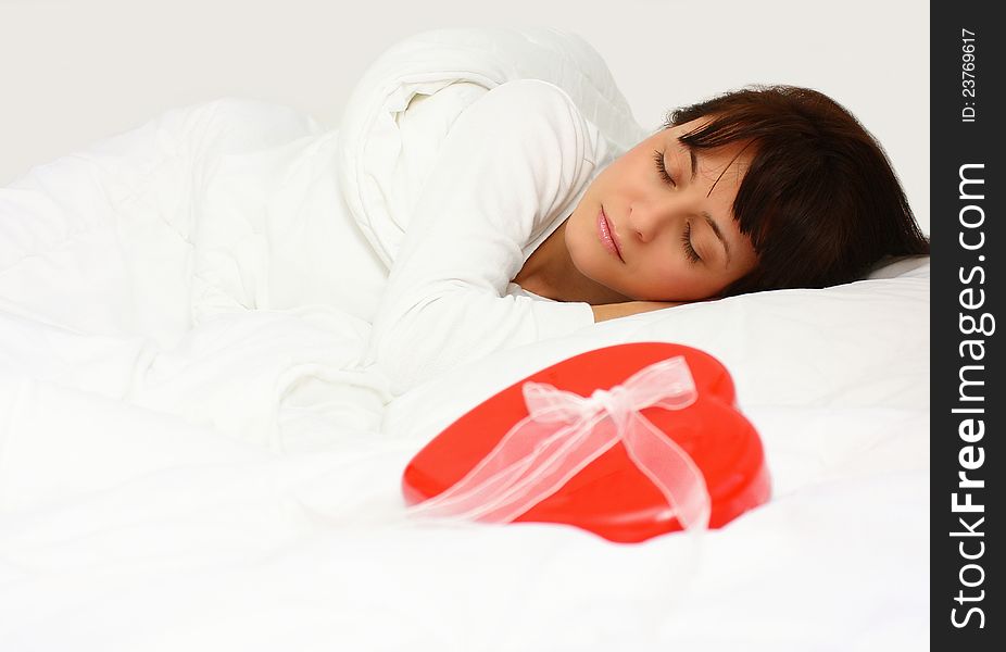 Beautiful woman sleeping in bed with a red gift heart shape next to her. Beautiful woman sleeping in bed with a red gift heart shape next to her