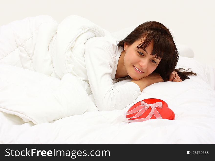 Surprised smiling woman finding a red gift with a heart shape in her bed in the morning