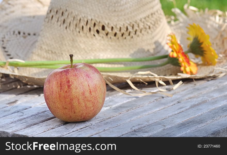 Apple placed front of  a straw hat in a garden in summer. Apple placed front of  a straw hat in a garden in summer