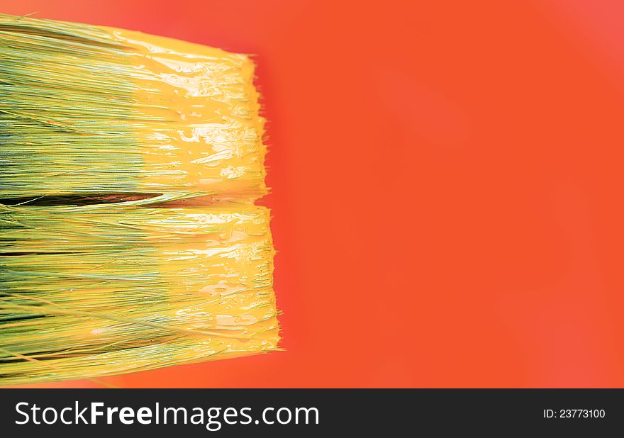 Tip of a paint brush with yellow paint and a orange canvas with copy space in the background. Tip of a paint brush with yellow paint and a orange canvas with copy space in the background