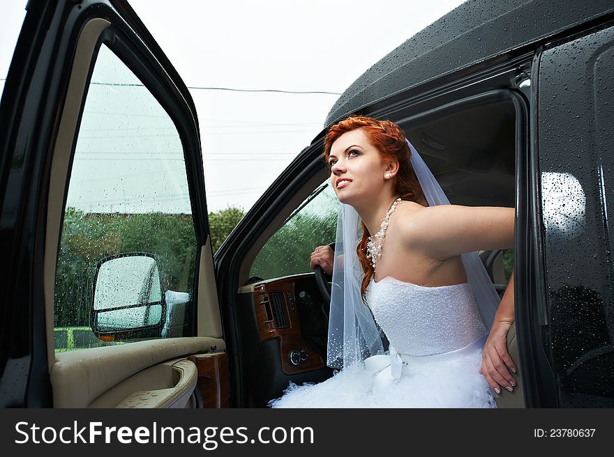 Beauty bride into big car in rainy day