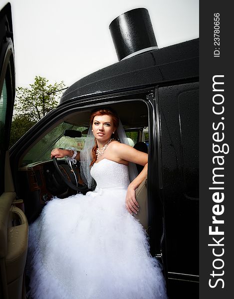 Beauty bride into big black car in rainy day