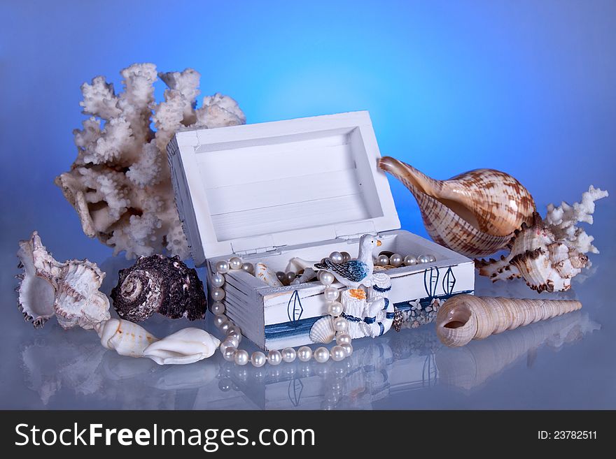 Box with seashells, coral and pearls. Blue background with reflection.