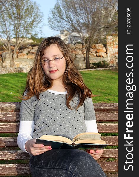 Young girl with glasses, sitting in the park and reading a book. Young girl with glasses, sitting in the park and reading a book