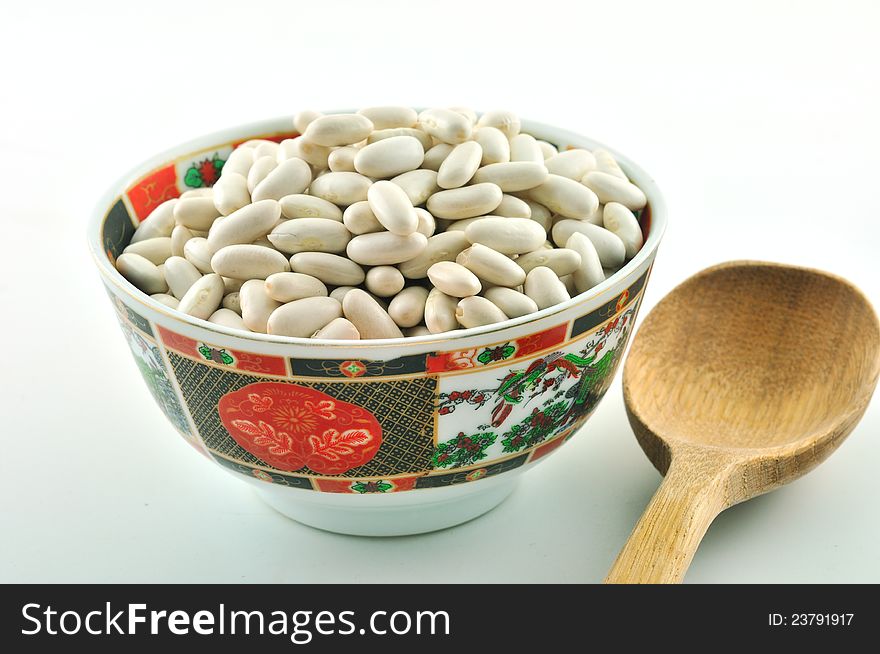 Ceramic bowl decorated with colored fruits full of white beans and wooden spoon. Ceramic bowl decorated with colored fruits full of white beans and wooden spoon