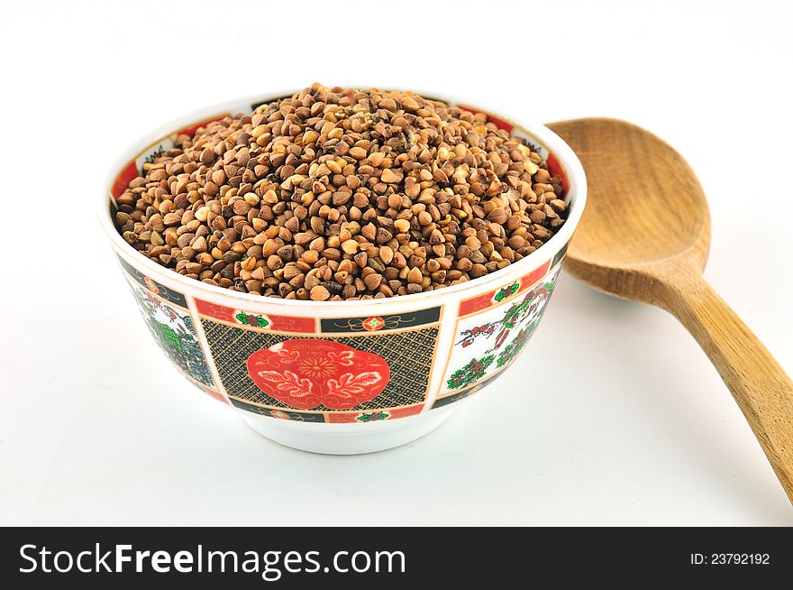 Ceramic bowl decorated with a color full of buckwheat, and a wooden spoon next to. Ceramic bowl decorated with a color full of buckwheat, and a wooden spoon next to