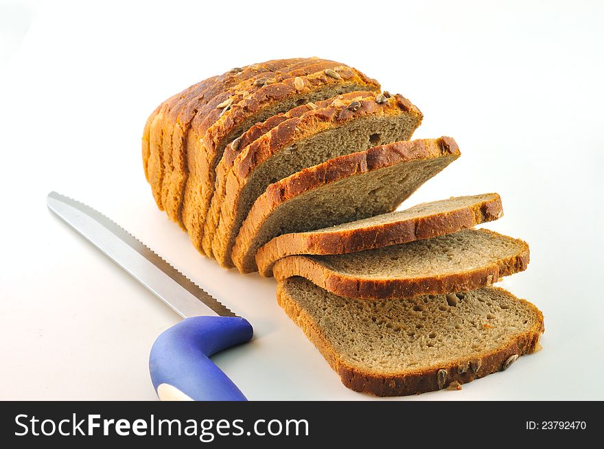 A loaf of rustic bread with sunflower seeds and a knife for cutting bread with a blue pen on the table, against a white background. A loaf of rustic bread with sunflower seeds and a knife for cutting bread with a blue pen on the table, against a white background