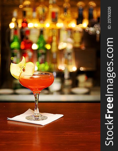 Red cocktail with piece of apple standing on bar counter