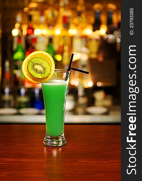 Green cocktail with piece of kiwi standing on bar counter