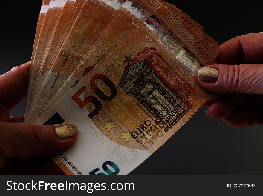 Wad of money of 50 euro banknotes in female hands, isolated on a grey background. Woman holding euro money. Close up view.