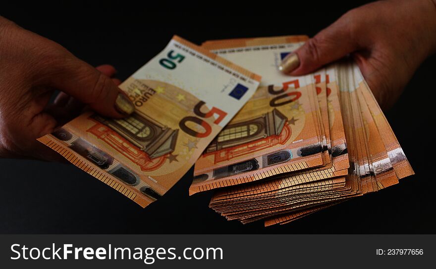 Woman takes a banknote from a bundle of money of 50 euro banknotes on a grey background. Woman holding euro money in hands.