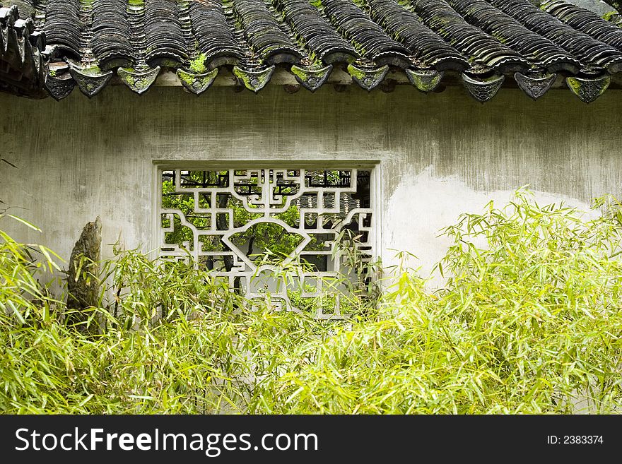 A beautiful window in a secluded Chinese garden in Suzhou with bamboo and moss covered tiles. A beautiful window in a secluded Chinese garden in Suzhou with bamboo and moss covered tiles.