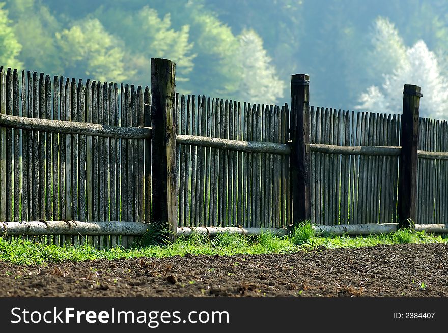 Old fence in the midst of brown field and trees