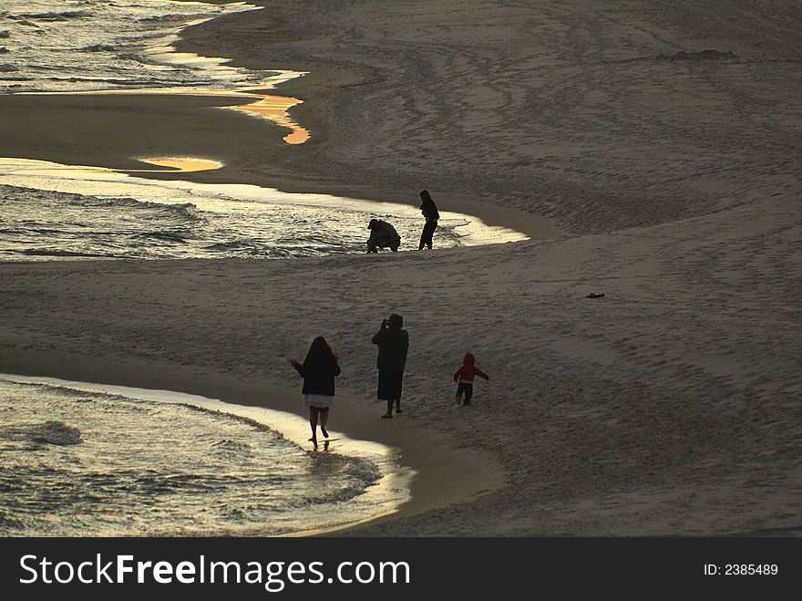 Sunset with golden ray on edge of water by the sandy beach with a family walking along the beach. Sunset with golden ray on edge of water by the sandy beach with a family walking along the beach