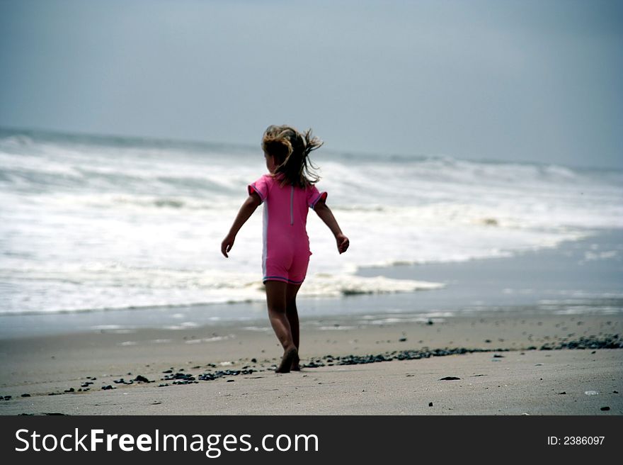 Portrait of a little girl walking towards the sea in a pink bathing suit