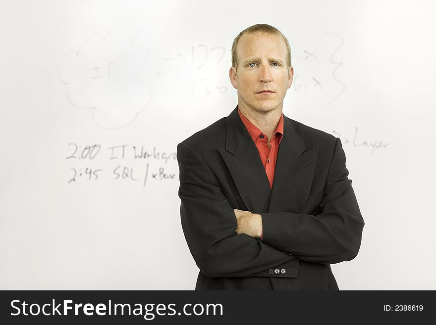 A businessman stands confidently in front of writing board with his arms crossed. A businessman stands confidently in front of writing board with his arms crossed