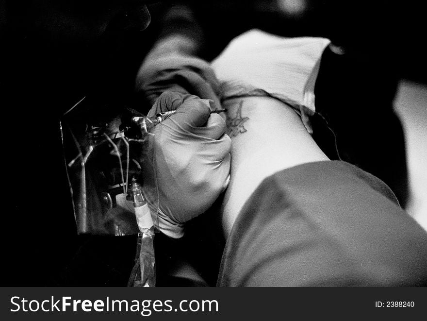 Tattoo artist inking a tattoo on a hip - in black and white. Tattoo artist inking a tattoo on a hip - in black and white