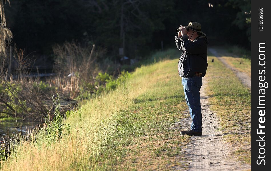 Man with binoculars looking out over pond in the morning