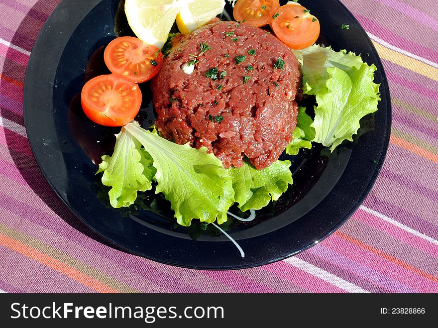 Raw ground beef with vegetables on a black dish