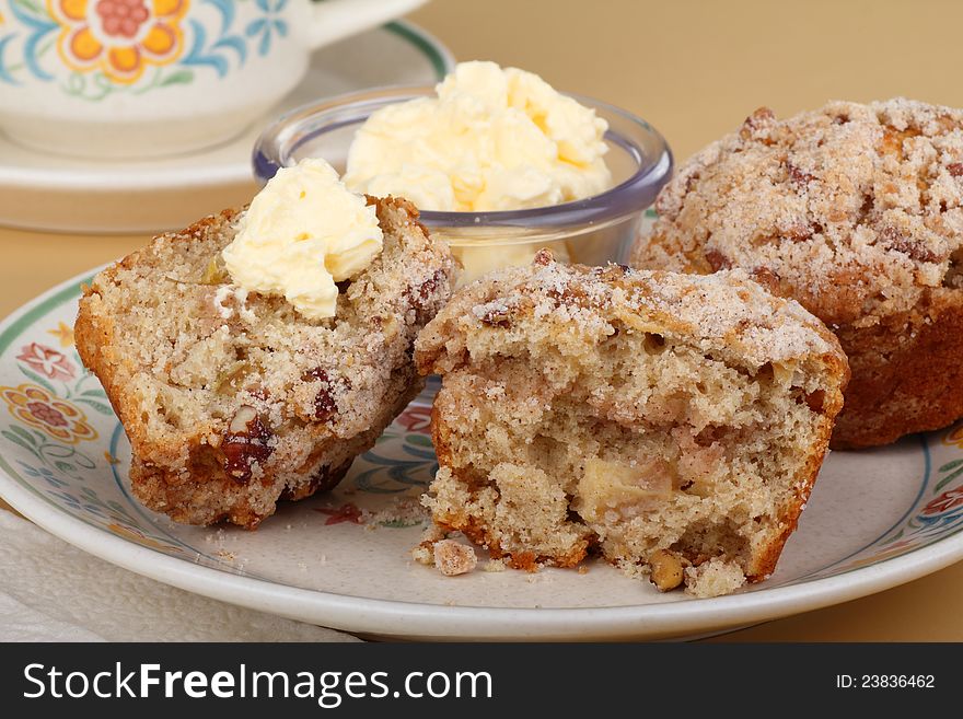 Two nut muffins, one cut in half with butter, on a plate. Two nut muffins, one cut in half with butter, on a plate