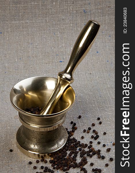 Brass mortar & pestle set with black pepper grain on sackcloth background. Brass mortar & pestle set with black pepper grain on sackcloth background