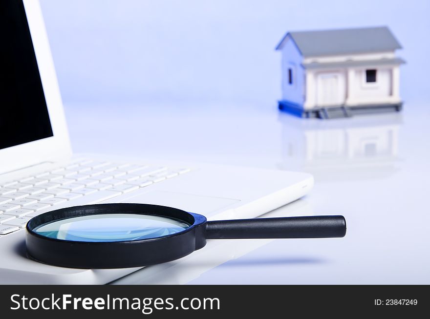 Black magnifying glass on laptop and a model house. Black magnifying glass on laptop and a model house
