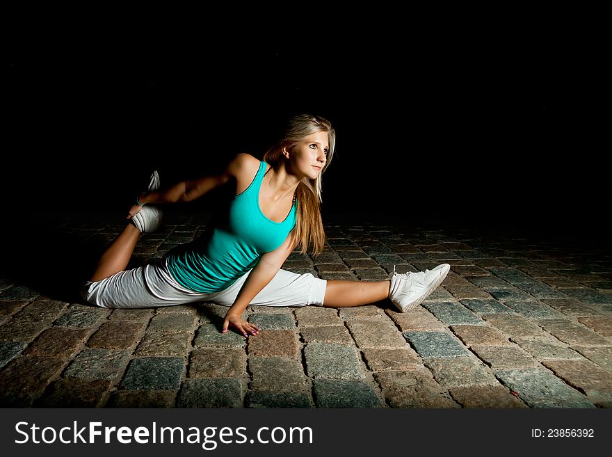 Beautiful blonde girl training at night on old pavement made of old stone tiles. Picture with black copy space. Beautiful blonde girl training at night on old pavement made of old stone tiles. Picture with black copy space.