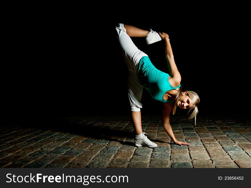 Beautiful blonde girl training at night on old pavement made of old stone tiles. Picture with black copy space. Beautiful blonde girl training at night on old pavement made of old stone tiles. Picture with black copy space.