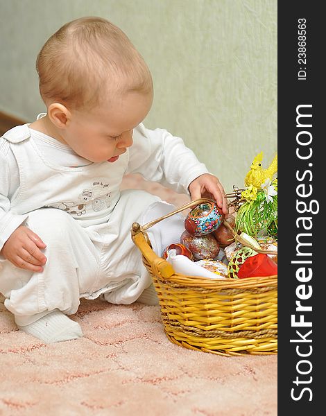 The kid near a basket with colored eggs sits. The kid near a basket with colored eggs sits