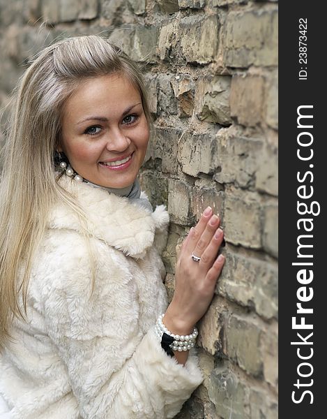 Young Happy Woman In Fur Coat Near an Old Brick Wall. Young Happy Woman In Fur Coat Near an Old Brick Wall