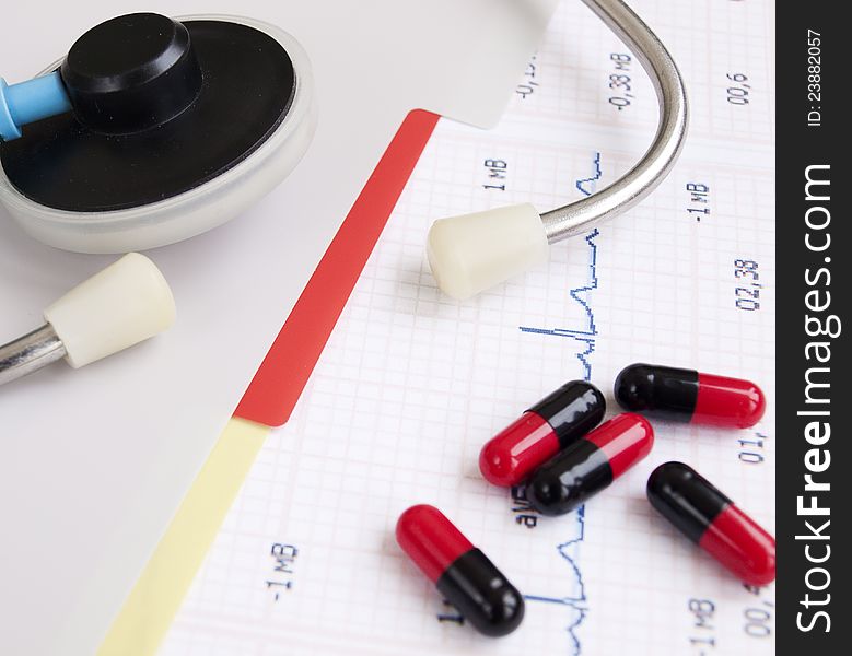 Stethoscope and pills on a printout of a heartrate graph. Stethoscope and pills on a printout of a heartrate graph