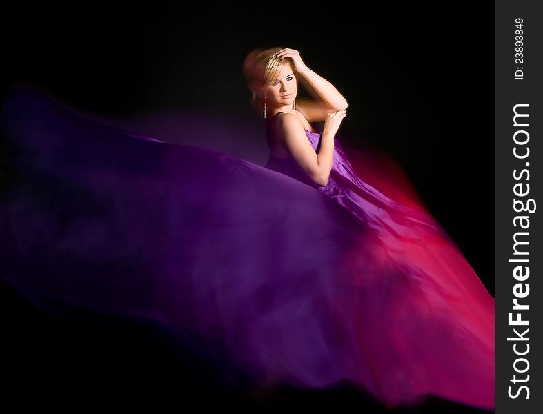 Beautiful blonde in the purple dress from flying fabric on a black background. Beautiful blonde in the purple dress from flying fabric on a black background