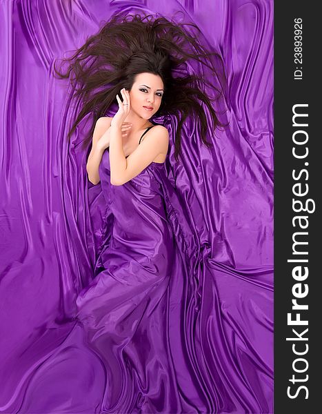 Beautiful girl with long dark hair lying against a background of purple silk. Beautiful girl with long dark hair lying against a background of purple silk