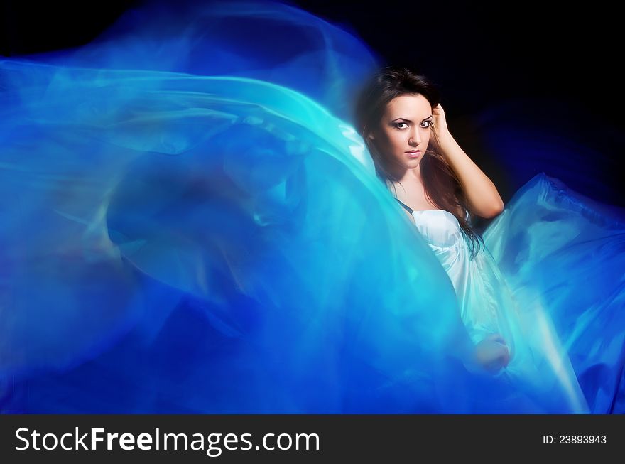 Beautiful girl in the blue dress from flying fabric on a black background