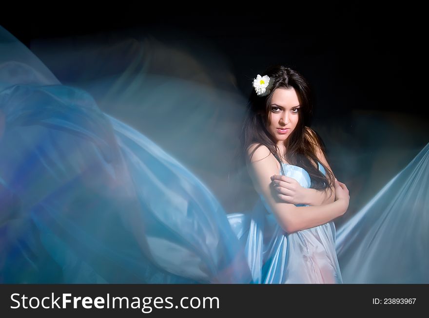Beautiful girl in the blue dress from flying fabric on a black background