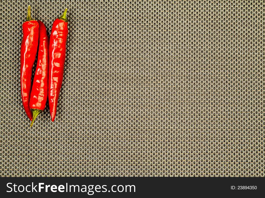 Three red hot peppers on a beige and black background. Three red hot peppers on a beige and black background